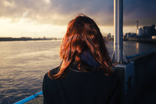 istock Woman admiring sunset over river in city 526093249