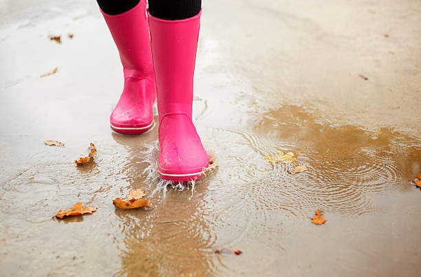 istock Woman with pink rubber boots walking through water puddle 526112929
