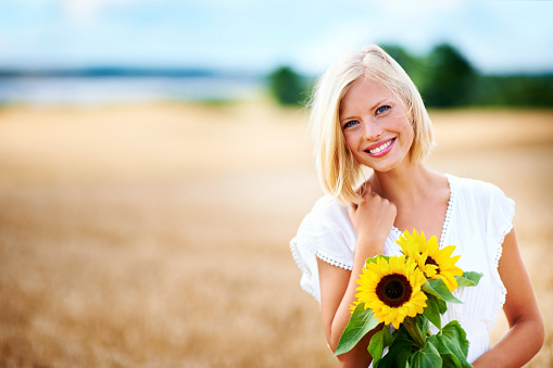 Gorgeous young woman smiling in a wheat field while holding some sunflowers