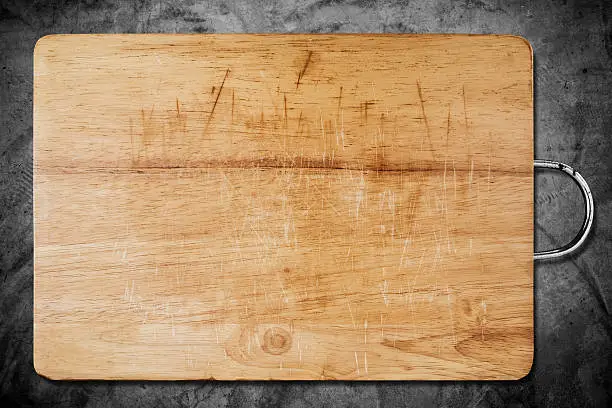 Old scratched wooden cutting board, on dark concrete texture