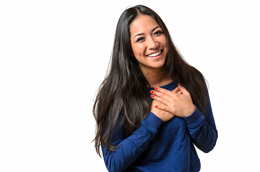 Young woman showing her heartfelt gratitude and thanks clasping her hands to her heart with a pleased smile