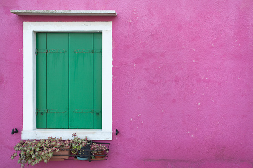 Burano, Italy - January 27, 2016: closed green balcony from a pink painted house in a cloudy winter day from a secondary street in Burano island, Venice