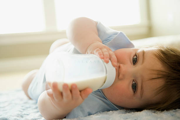 baby мальчик пьет молоко из бутылки молока - baby lying down indoors one person стоковые фото и изображения