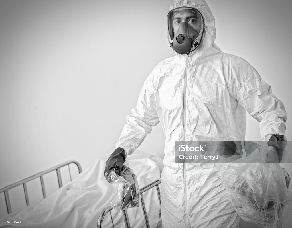 Man in Hazmat Suit Carries Contaminated Items in Plastic Bags A man in a hazmat suit carries contaminated items away in plastic bags from a deceased patient in hospital. Adult Stock Photo