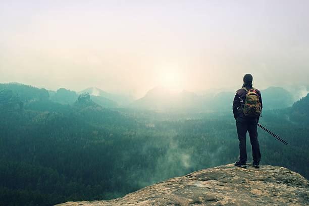 istock Tourist with backpack and poles on cliff watching into valley 526153568