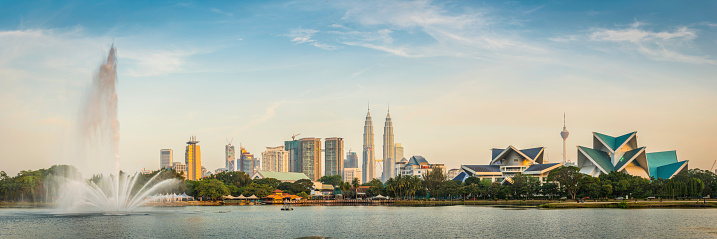 Warm sunset light illuminating the Petronas Towers and downtown skyscrapers of Kuala Lumpur, Malaysia's vibrant capital city, as they soar over the leafy foliage and fountains Taman Tasik Titiwangsa lake. ProPhoto RGB profile for maximum color fidelity and gamut.