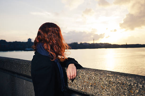 istock Woman admiring sunset over river in city 526179367