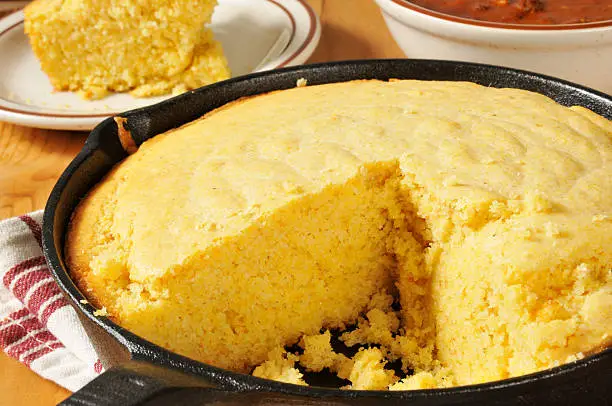 Corn bread in a cast iron skillet with a bowl of chili in the background