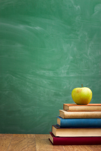 School books with apple on desk over green  school board background