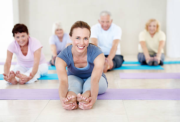 My student's wellness is my passion Portrait of an attractive woman leading a group of happy seniors in a yoga class touching toes stock pictures, royalty-free photos & images