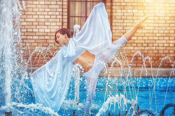 Young beautiful girl in white clothes dancing in a fountain