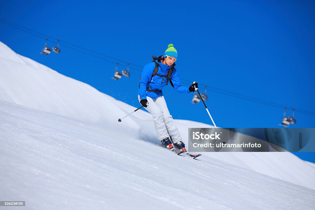 Mid adult women snow skier skiing on sunny ski resorts Mid adult women snow skier skiing, enjoying on sunny ski resorts Livigno. Skiing carving at high speed, chunks of snow flying against the beautiful blue sky in the background. Shot with Canon 5DMarkIII, developed from RAW, Adobe RGB color profile. Shallow DOF for soft background. Active Lifestyle Stock Photo