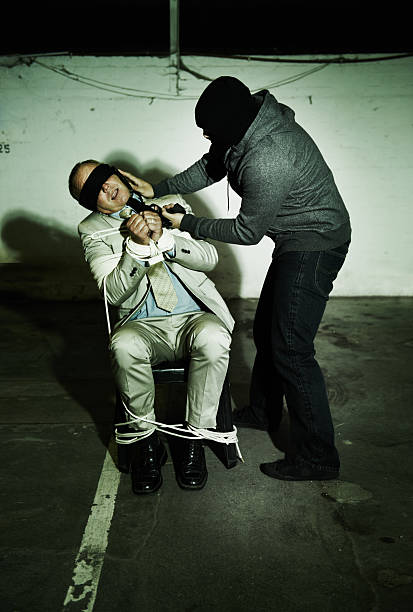 A bound and gagged businessman being told to talk on a cellphone while being held at gunpoint
