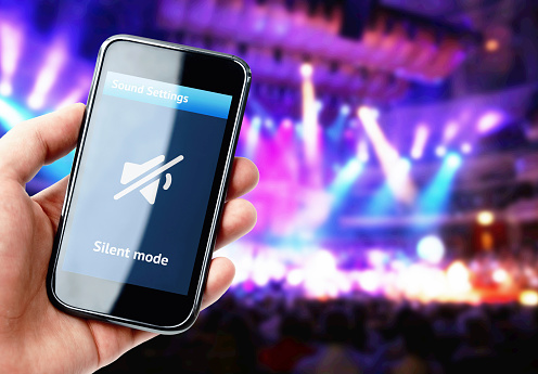 Hand holding smartphone with mute sound on the screen during concert