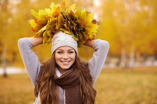 Portrait of a beautiful young woman holding a bunch of leaves in the park on an autumn's day
