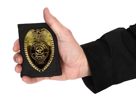 Here is man's hand, holding golden police officer badge.