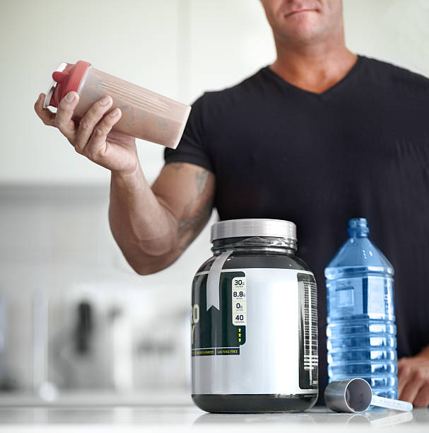 Building muscle with protein shakes Cropped image of a bodybuilder making himself a protein shake water athlete competitive sport vertical stock pictures, royalty-free photos & images