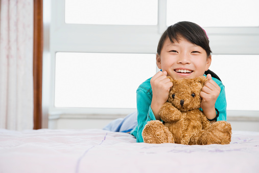 Girl (8-9) holding teddy bear, smiling, portrait