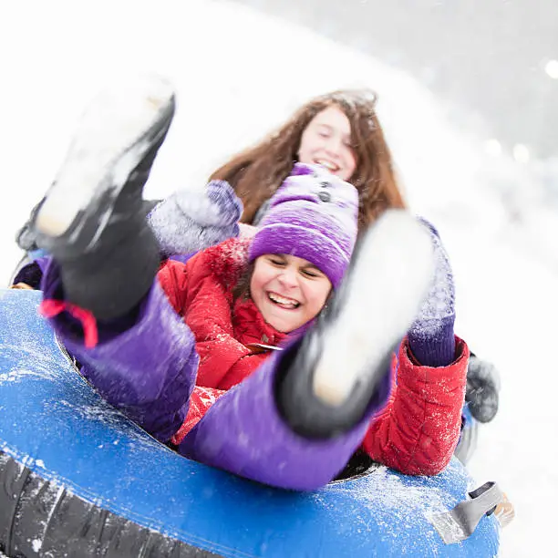 Two sisters, teenager girl and little girl, sliding at the slope and have fun with snowtubing at the winter resort 