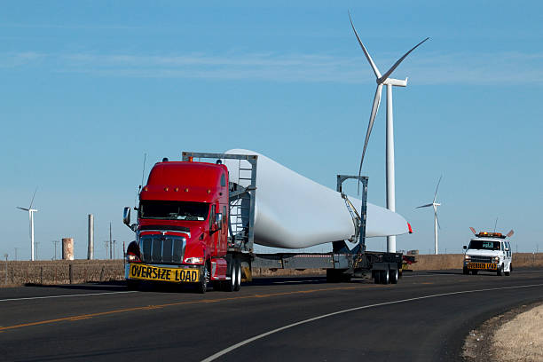 Just outside the small town of Vega and west of Amarillo, an oversized load of a wind turbine blade is carried by a semi-truck which drives past huge, modern, curved bladed, wind turbines turning in high winds on the Wildorado Wind Ranch and on nearby farm lands in Texas.