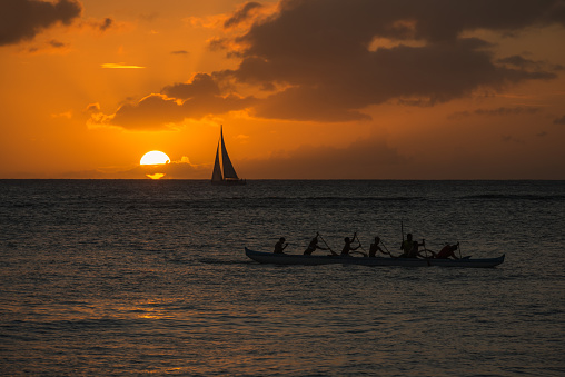 Honolulu, USA - November 13, 2015: A sail boat off Waikiki at sunset with the Saint Francis rowing team passing by. 