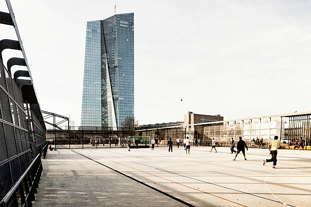 Frankfurt, Germany - November 23, 2014: Tower of the new European Central Bank. It is the headquarters of ECB under construction in Frankfurt, Germany. The 500 million euro project will be completed at winter 2014. In front you see a sports ground . People are playing soccer there.