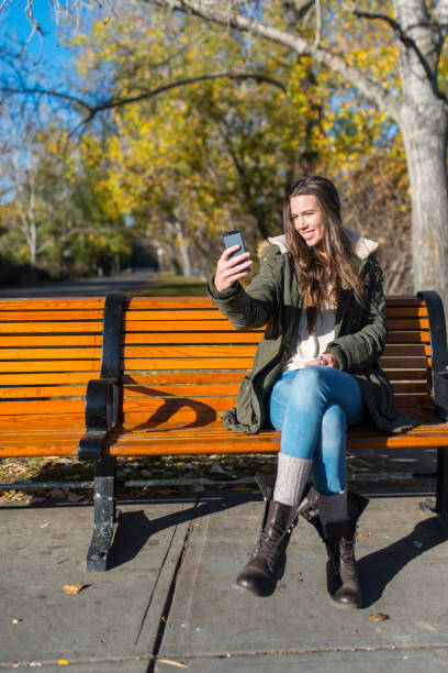 istock Young woman looks at smart phone on park bench 526281781
