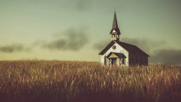 Old abandoned white wooden chapel on prairie at sunset with cloudy sky.