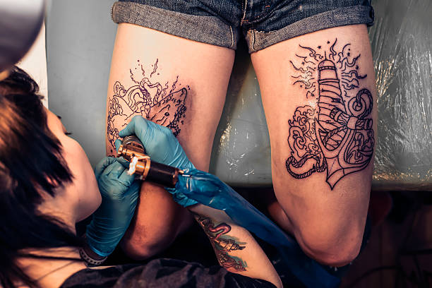 Top view of making tattoo on legs in salon. Showing processing of making a tattoo by woman artist. Tattooist machine,gun. Free space to fill,text.