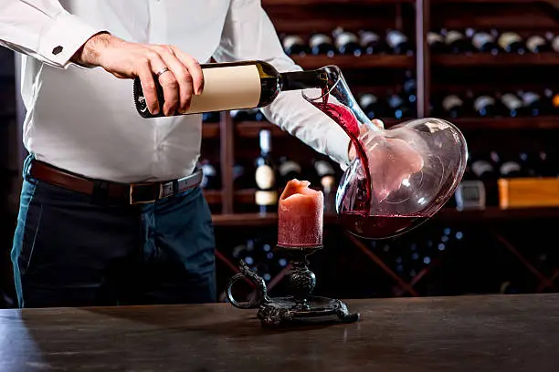Sommelier pouring wine to the decanter in the wine cellar