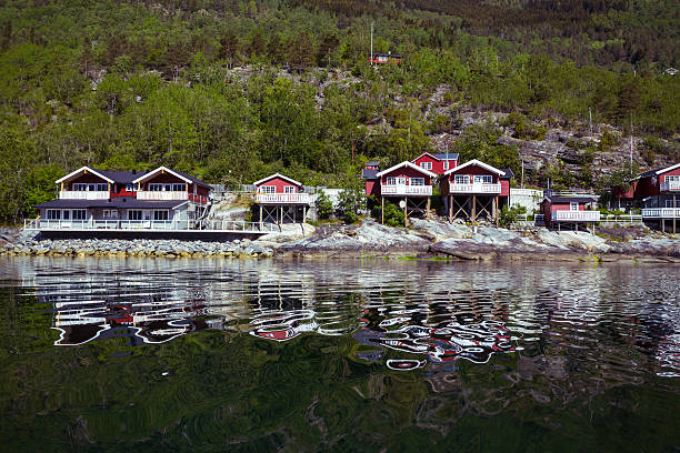 rorbuer - traditional norwegian red wooden house to stand at the lakeside and mountains in the distance, norway