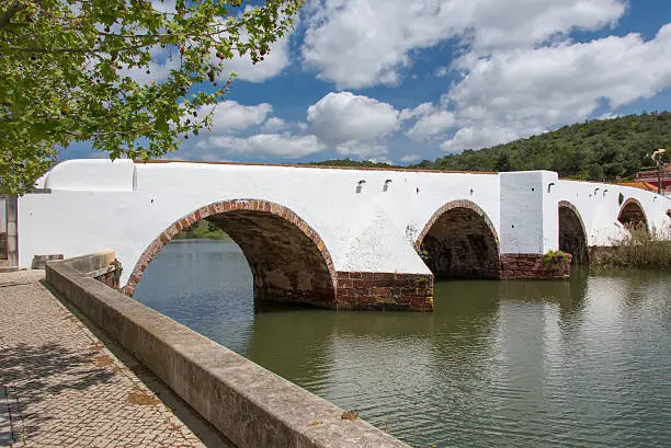 The white Ponte Romana or Roman bridge crossing the river Arade in the medieval village of Silves in the Algarve region of Portugal.