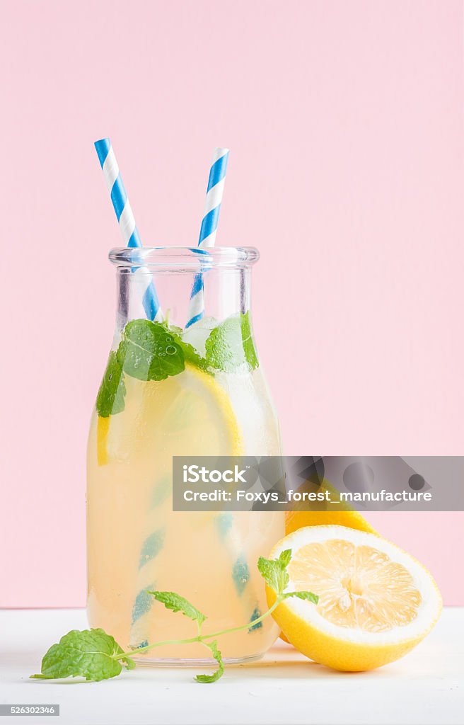 Bottle of homemade lemonade with mint, ice, lemons, paper straws Bottle of homemade lemonade with ice and lemons, paper straws and pastel pink background, selective focus Lemonade Stock Photo