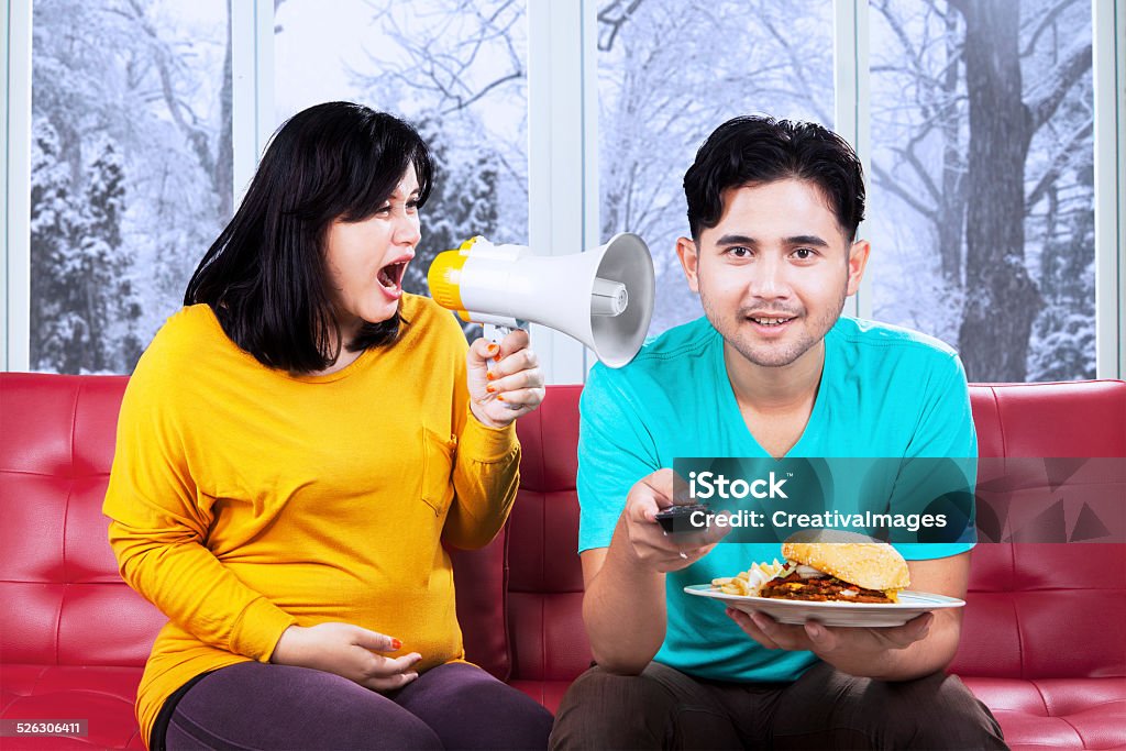 Furious pregnant mother on her husband Portrait of pregnant woman yelling with a megaphone on her husband at home with winter background Adult Stock Photo