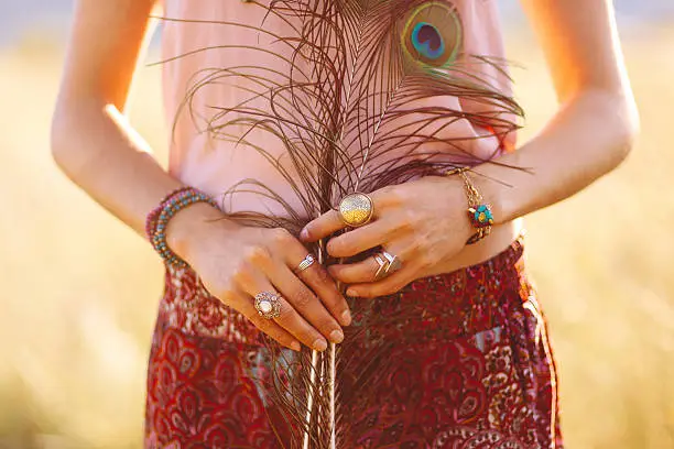 Close-up image of a woman's hands, wearing fashionable vintage oriental jewelry, holding peacock feathers. Shot in pastel, cross processed tones of film emulation, with Canon full frame camera EOS 5d mark 2 with large aperture 85mm prime lens  at f1,8.