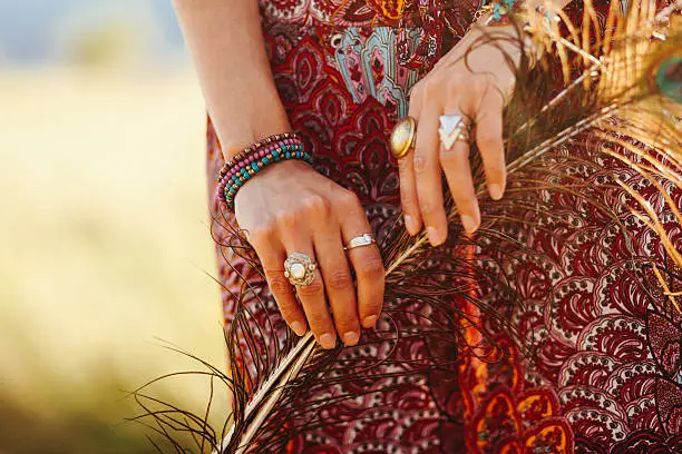 Close-up image of a woman's hands, wearing fashionable vintage oriental jewelry, holding peacock feathers. Shot in pastel, cross processed tones of film emulation, with Canon full frame camera EOS 5d mark 2 with large aperture 85mm prime lens  at f1,8.