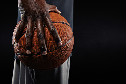 Close-up of a hand of basketball player holding a ball against black background.