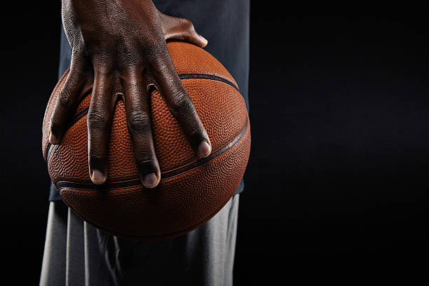 Hand of basketball player holding a ball Close-up of a hand of basketball player holding a ball against black background. basketball player photos stock pictures, royalty-free photos & images