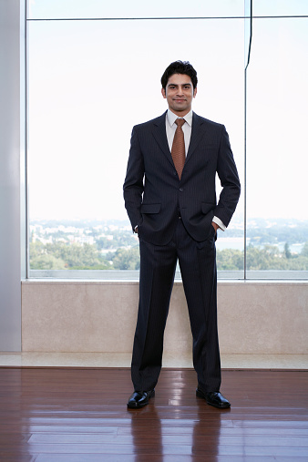 Full length portrait of confident young businessman with hands in pockets at office