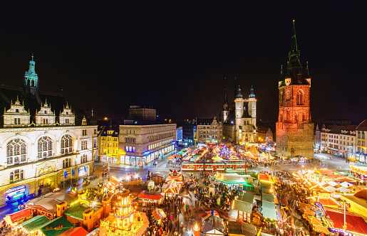 Elevated view over the christmas market at the market square of Halle (an der Saale) with the illuminated Red Tower (Rotem Turm), the Market Church of Our Dear Lady (Marktkirche Unser Lieben Frauen), the George Frideric Handel statue (Hände-Denkmal) and the Town Hall (Stadthaus) on the left.