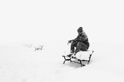 Lonely man sitting on bank in winter
