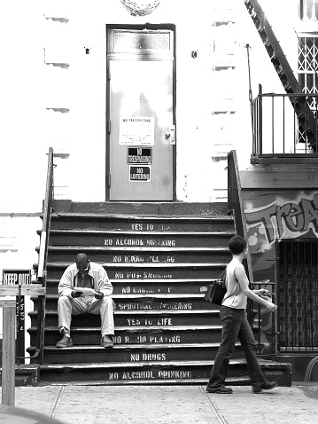 New York City, NY, USA - November 2, 2001: Man reads on steps of 25 St Marks Pl NYC. Woman walks by him. East Village, NYC.