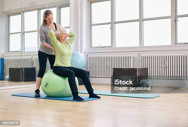 Female Trainer Helping Senior Woman Exercising In Gym Stock Photo - Download Image Now