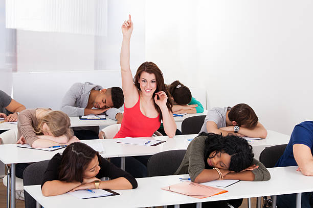 Smiling Student Raising Hand With Classmates Sleeping At Desk Portrait of smiling college student raising hand with classmates sleeping at desk in classroom male college student sleeping through lecture stock pictures, royalty-free photos & images