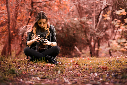 Woman holds a tlr camera and sitting in woods.