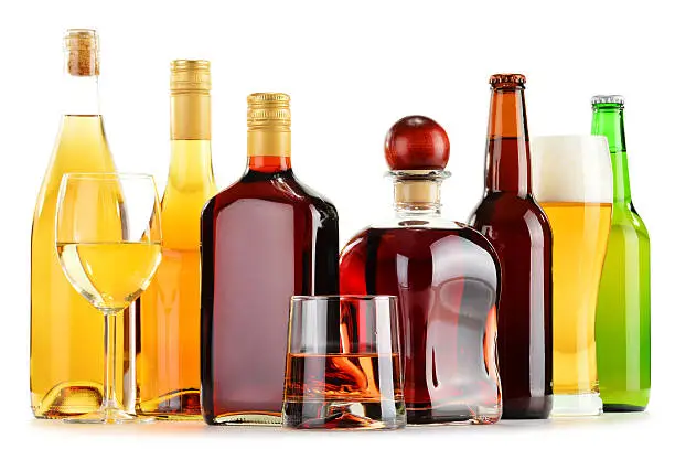 Bottles and glasses of assorted alcoholic beverages isolated on white background