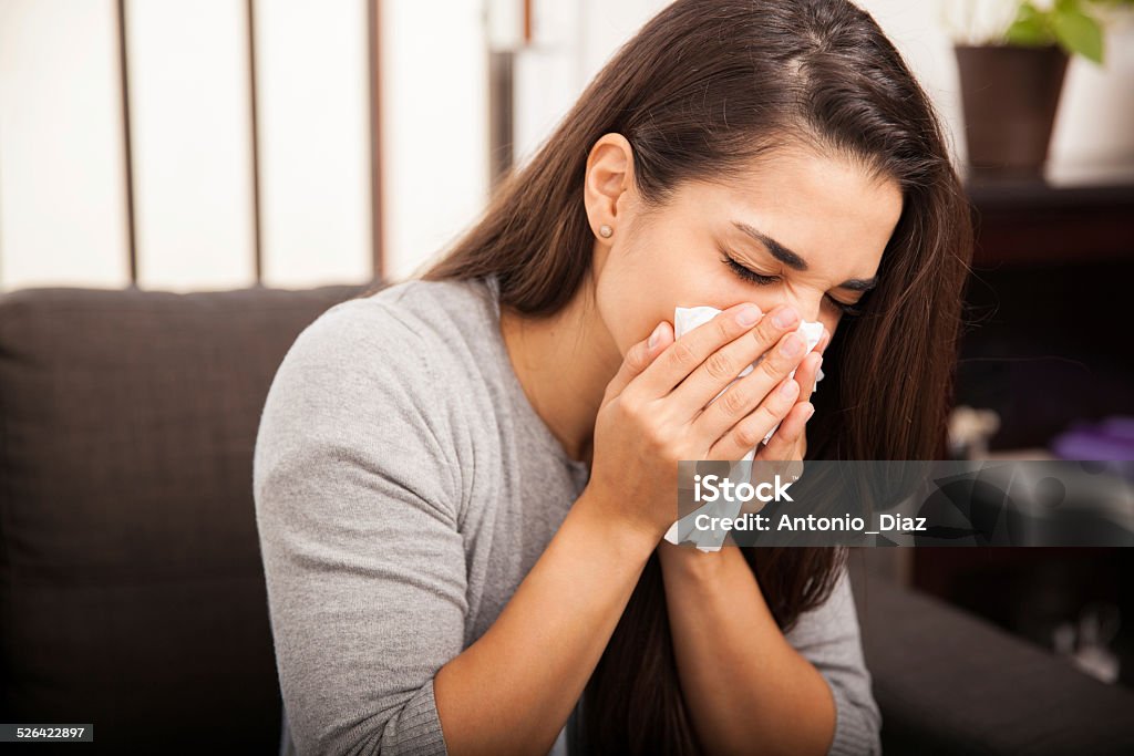 Cute girl blowing her nose Portrait of a cute young brunette blowing her nose after catching a cold 20-29 Years Stock Photo