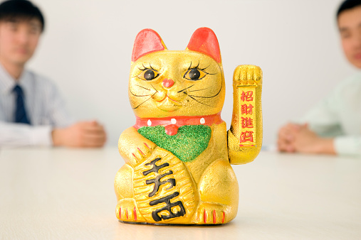 Chinese Cat Bringing Good Luck. Items on the Shelf. Glare of light on objects. Gold-colored toy.