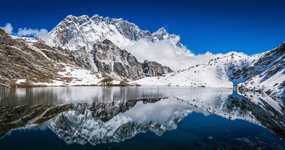 The jagged sawtooth ridge of Nuptse (7861m) and snow capped spire of Lhotse (8516m) reflecting in the tranquil blue waters of a high altitude lake deep in the picturesque Himalaya mountain wilderness of the Everest National Park, a UNESCO World Heritage Site. ProPhoto RGB profile for maximum color fidelity and gamut.