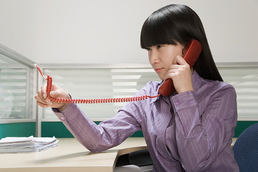 Businesswoman looking at unplugged cord of telephone receiver